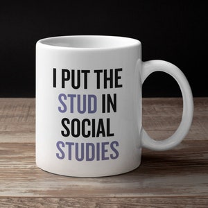 Puede incluir: Taza de café de cerámica blanca con texto negro que dice "I put the stud in social studies".