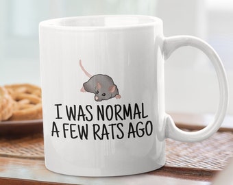 May include: White ceramic coffee mug with a black and gray rat illustration and the text "I was normal a few rats ago".