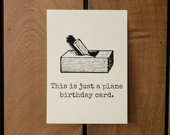 Puede incluir: Una tarjeta blanca con una ilustración en blanco y negro de un cepillo de carpintero. El texto en la tarjeta dice "This is just a plane birthday card."
