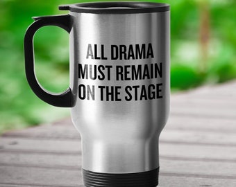 Op de afbeelding: Een zilveren reistumbler met een zwarte handgreep en deksel. Op de tumbler staat de tekst "ALL DRAMA MUST REMAIN ON THE STAGE".