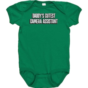 May include: Green baby onesie with the text "Daddy's Cutest Camera Assistant" in white.