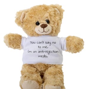 May include: A brown teddy bear wearing a white t-shirt with the text "You can't say no to me. I'm on anti-rejection meds."