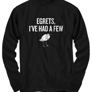 May include: Black long-sleeve shirt with the text "EGRETS, I'VE HAD A FEW" in white. Below the text is a watercolor illustration of a white egret with blue and yellow accents. The shirt is made of a soft material.