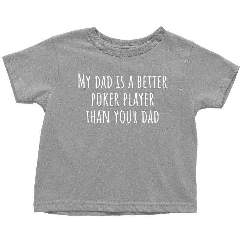 May include: Gray short-sleeved t-shirt with the text "My dad is a better poker player than your dad" in white.