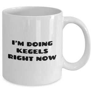 May include: White ceramic coffee mug with black text that reads "I'm doing Kegels right now".
