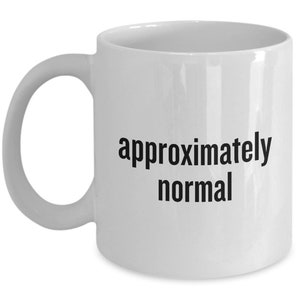 Könnte beinhalten: Weiße Keramik-Kaffeetasse mit schwarzem Text, der "ungefähr normal" lautet.