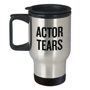 May include: A silver travel mug with a black lid and handle. The mug has the text "ACTOR TEARS" printed in black on the front.