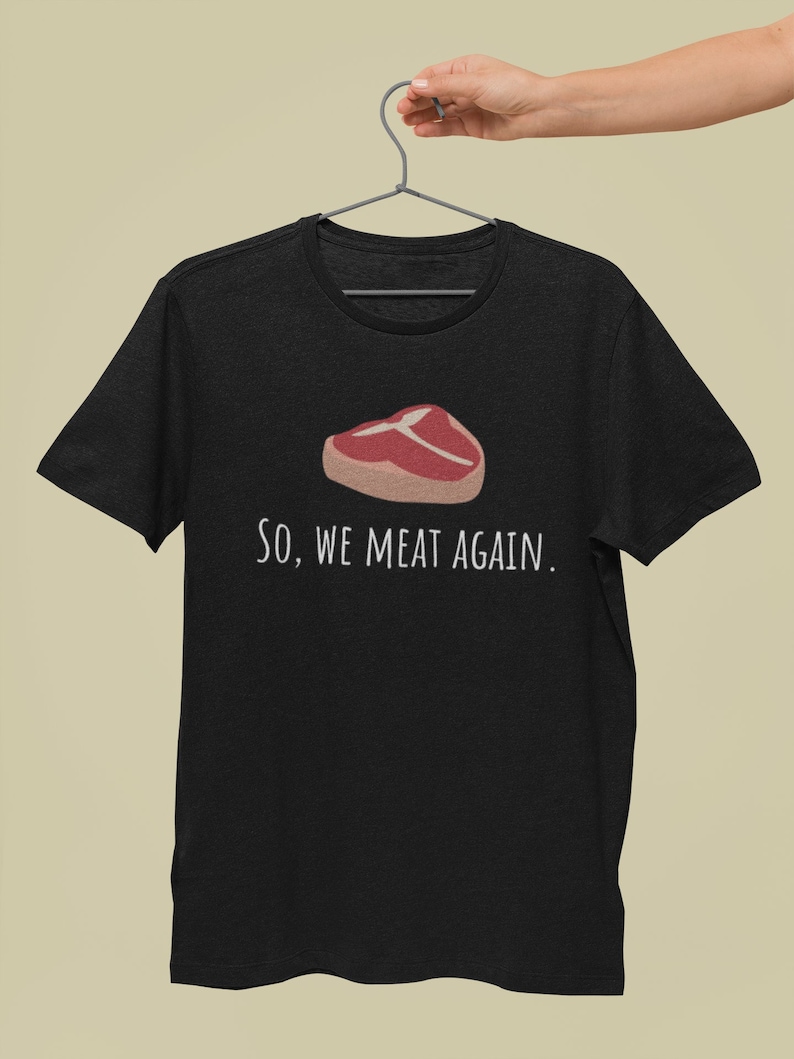 May include: Black t-shirt with a white graphic of a steak and the text "So, we meat again."