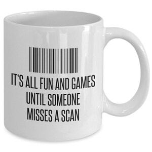 May include: White ceramic mug with a black barcode design and the text "IT'S ALL FUN AND GAMES UNTIL SOMEONE MISSES A SCAN". The mug has a curved handle and is suitable for hot or cold beverages.