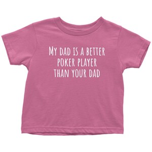 May include: Pink toddler t-shirt with white text that reads "My dad is a better poker player than your dad."