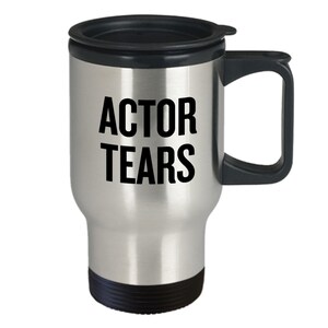 May include: A silver travel mug with a black lid and handle. The mug has the text "ACTOR TEARS" printed on it in black.