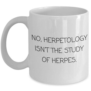 May include: White ceramic coffee mug with black text that reads "NO, HERPETOLOGY ISN'T THE STUDY OF HERPES."