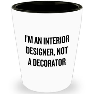 May include: White shot glass with a black rim. The text "I'M AN INTERIOR DESIGNER, NOT A DECORATOR" is printed in bold black letters on the front of the glass.