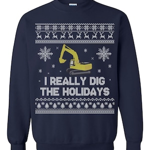 Peut inclure: Sweat-shirt bleu marine avec un motif festif. Il présente une excavatrice jaune, des flocons de neige et le texte "I REALLY DIG THE HOLIDAYS" en blanc. Le haut et le bas du sweat-shirt ont un motif de flocons de neige et de rennes blancs.