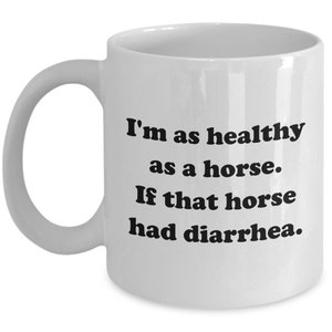 May include: White ceramic mug with a curved handle. The mug features the text: "I'm as healthy as a horse. If that horse had diarrhea." The text is in a bold, black font. A humorous gift idea.