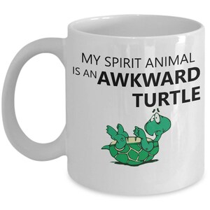 Może przedstawiać: Biały ceramiczny kubek do kawy z czarno-zielonym rysunkiem ż&oacute;łwia na plecach. Tekst na kubku brzmi "My spirit animal is an awkward turtle."