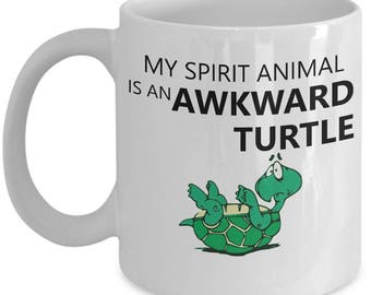 May include: White ceramic coffee mug with a black and green illustration of a turtle on its back. The text on the mug reads "My spirit animal is an awkward turtle."