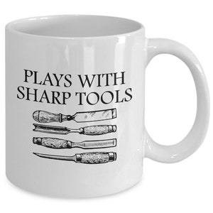 May include: White ceramic mug with a black graphic that says "Plays with Sharp Tools" and a drawing of four chisels.