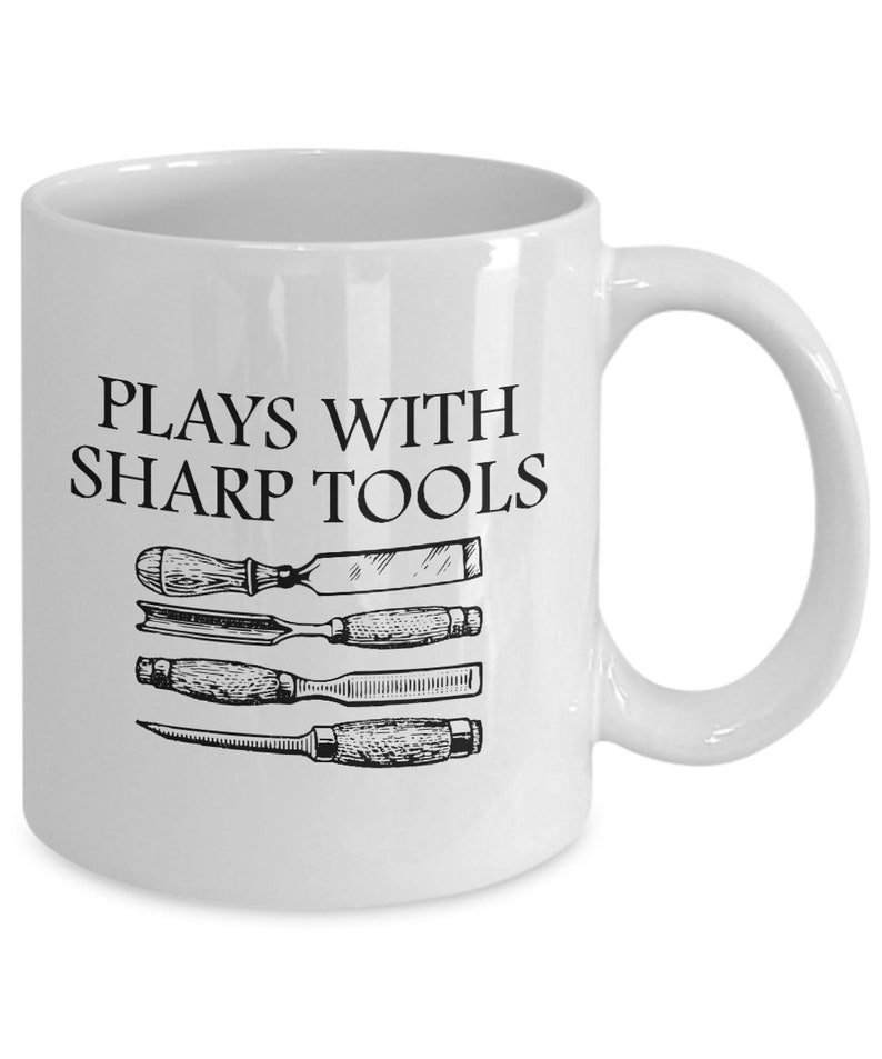 May include: White ceramic mug with a black graphic that says "Plays with Sharp Tools" and a drawing of four chisels.