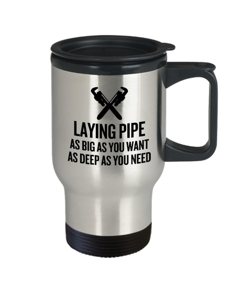 May include: A silver travel mug with a black lid and handle. The mug has a black graphic of two crossed wrenches and the text "Laying Pipe As Big As You Want As Deep As You Need".