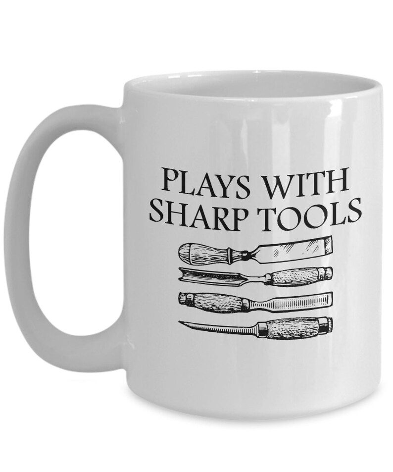 May include: White ceramic coffee mug with a black inscription that reads "Plays with sharp tools". The mug features a black and white illustration of four woodworking tools.
