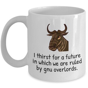 Puede incluir: Taza de cerámica blanca con una cabeza de ñu de dibujos animados y el texto: "I thirst for a future in which we are ruled by gnu overlords." La taza tiene un asa curva.