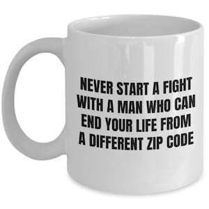 May include: White ceramic mug with a curved handle. The mug features black text that reads: "NEVER START A FIGHT WITH A MAN WHO CAN END YOUR LIFE FROM A DIFFERENT ZIP CODE."