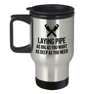 May include: A silver travel mug with a black lid and handle. The mug has a black graphic of two crossed wrenches and the text "Laying Pipe As Big As You Want As Deep As You Need".