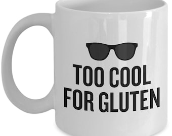 Könnte beinhalten: Weiße Keramik-Kaffeetasse mit einer schwarzen Grafik von Sonnenbrillen und dem Text "Too Cool For Gluten".