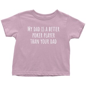 May include: A light purple t-shirt with the text "My dad is a better poker player than your dad" printed in white.