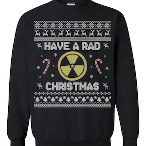 Puede incluir: Sudadera negra con un diseño festivo. El diseño incluye el texto "HAVE A RAD CHRISTMAS" con un símbolo de radiación, bastones de caramelo, copos de nieve y renos. La parte superior e inferior del diseño tienen un patrón repetitivo.