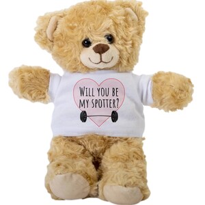 Könnte beinhalten: Ein brauner Teddybär, der ein weißes T-Shirt mit einem rosa Herz und dem Text "Willst du mein Spotter sein?" trägt. Das Herz enthält eine Langhantel.
