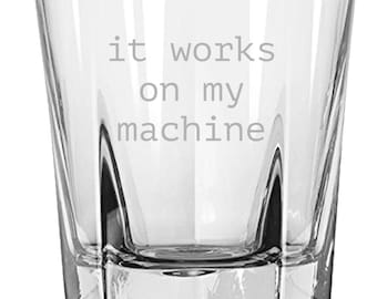 May include: A clear, faceted glass tumbler with the phrase "it works on my machine" etched in a gray font. The glass has a geometric design and is suitable for various beverages.