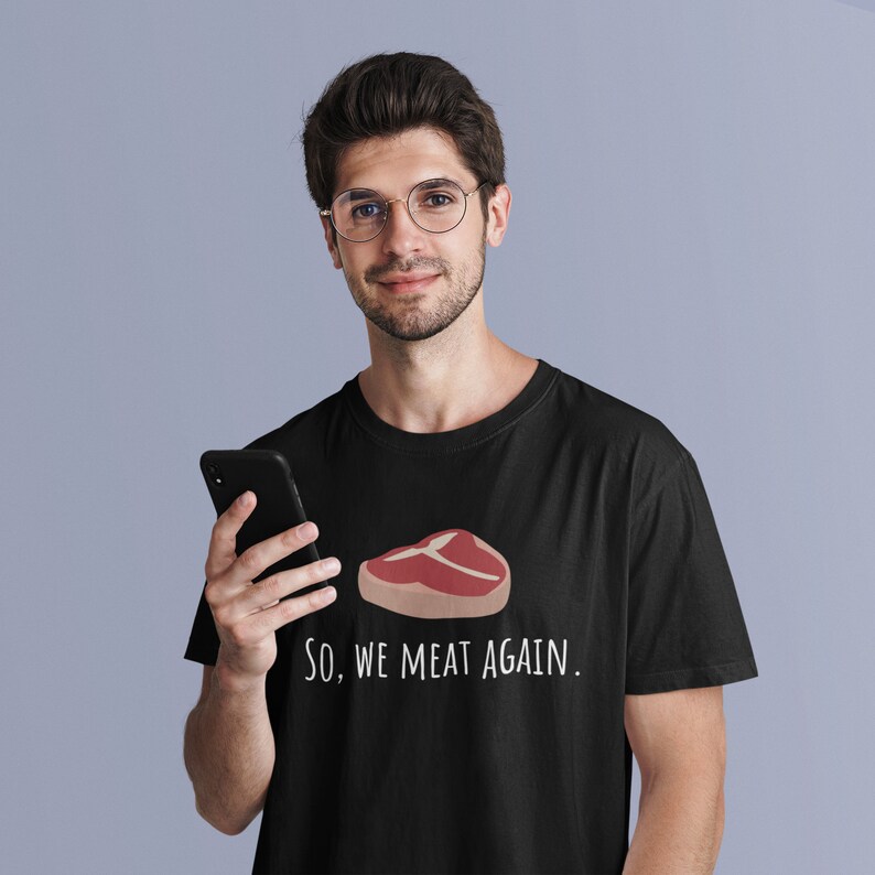 May include: A black t-shirt with a white graphic of a steak and the text "So, we meat again."
