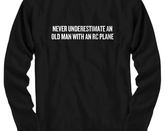 May include: Black long-sleeve shirt with the white text: "NEVER UNDERESTIMATE AN OLD MAN WITH AN RC PLANE." The shirt has a crew neck and long sleeves. The text is centered on the chest.