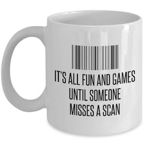 May include: White ceramic mug with a black barcode graphic and the text "IT'S ALL FUN AND GAMES UNTIL SOMEONE MISSES A SCAN". The mug has a curved handle and is suitable for hot or cold beverages.