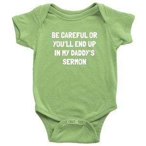 May include: A light green baby onesie with the text "BE CAREFUL OR YOU'LL END UP IN MY DADDY'S SERMON" printed in white.
