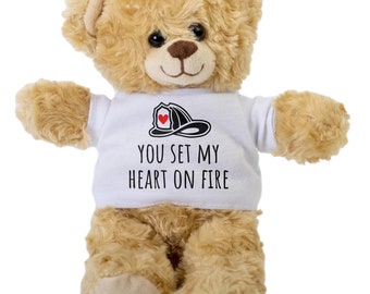 Może przedstawiać: Brązowy miś pluszowy w białej koszulce z czarnym nadrukiem hełmu strażaka i tekstem "You set my heart on fire".