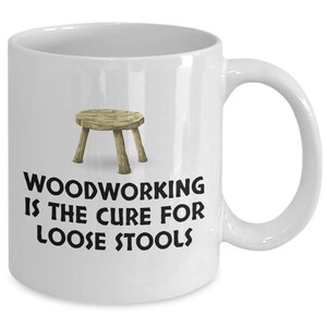 K&ouml;nnte beinhalten: Eine wei&szlig;e Keramik-Kaffeetasse mit einer Schwarzwei&szlig;-Illustration eines Holzhockers und dem Text "Woodworking is the cure for loose stools".