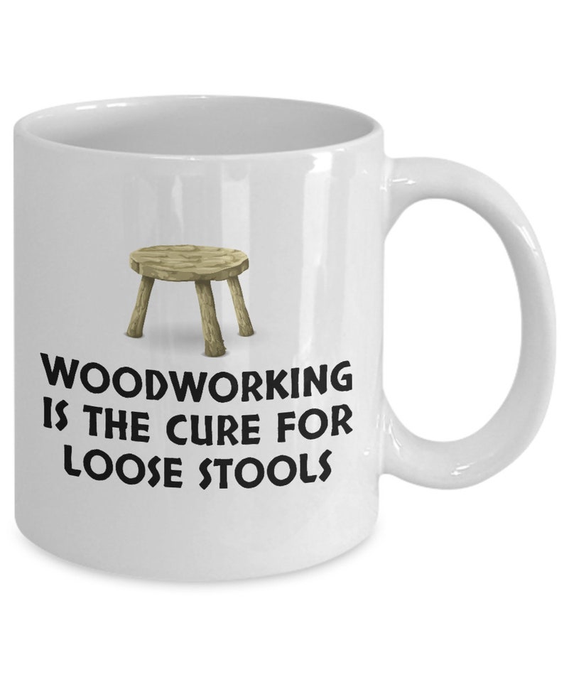 K&ouml;nnte beinhalten: Eine wei&szlig;e Keramik-Kaffeetasse mit einer Schwarzwei&szlig;-Illustration eines Holzhockers und dem Text "Woodworking is the cure for loose stools".