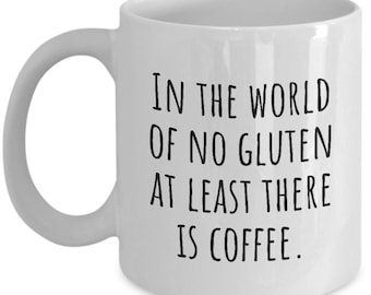 Puede incluir: Taza de café de cerámica blanca con texto negro que dice "En el mundo sin gluten al menos hay café."