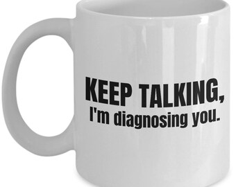 May include: White ceramic coffee mug with black text that reads "KEEP TALKING, I'm diagnosing you."