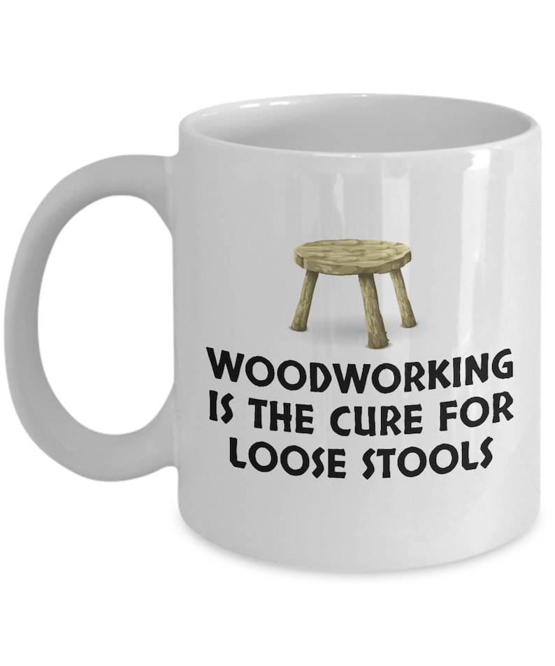 K&ouml;nnte beinhalten: Wei&szlig;e Keramik-Kaffeetasse mit einer Schwarzwei&szlig;-Illustration eines Holzhockers und dem Text "Woodworking is the cure for loose stools".