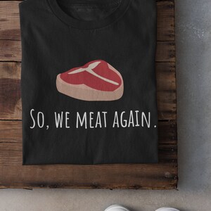 May include: Black t-shirt with a white graphic of a steak and the text "SO, WE MEAT AGAIN."