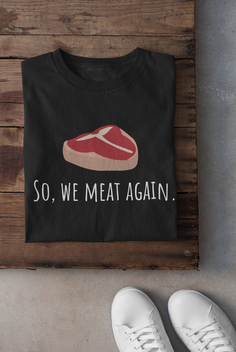 May include: Black t-shirt with a white graphic of a steak and the text "SO, WE MEAT AGAIN."