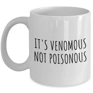 May include: White ceramic coffee mug with black text that reads "It's Venomous Not Poisonous".