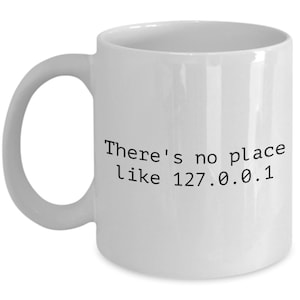 May include: White ceramic coffee mug with black text that reads "There's no place like 127.0.0.1"
