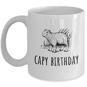 May include: White ceramic coffee mug with a black line drawing of a capybara and the text "CAPY BIRTHDAY" printed on the front.
