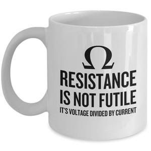 Puede incluir: Taza de café de cerámica blanca con un gráfico negro que dice "La resistencia no es fútil. Es voltaje dividido por corriente." El gráfico también incluye la letra griega omega, el símbolo de la resistencia.