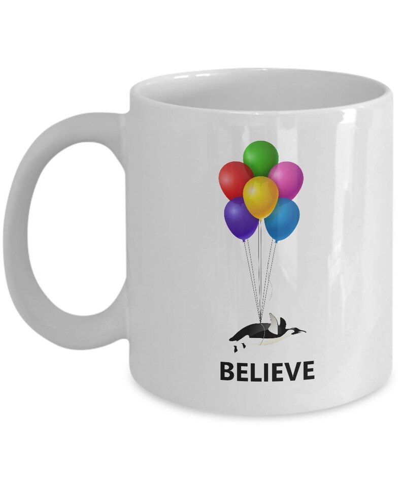 May include: White ceramic mug with a penguin holding onto colorful balloons. The text "BELIEVE" is printed on the mug.